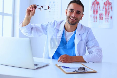 Téléchargez les photos : Portrait d'un médecin avec un ordinateur portable assis au bureau médical - en image libre de droit