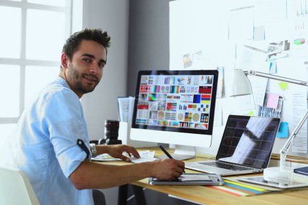 Photo for Portrait of young designer sitting at graphic studio in front of laptop and computer while working online - Royalty Free Image