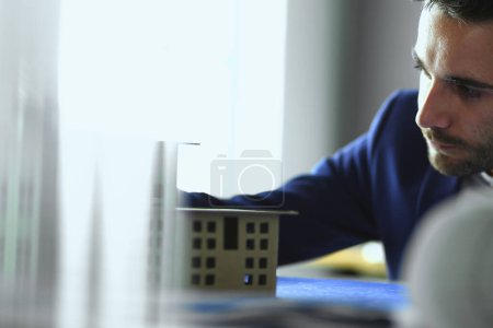 Téléchargez les photos : Homme d'affaires tenant maison miniature à portée de main debout dans le bureau - en image libre de droit