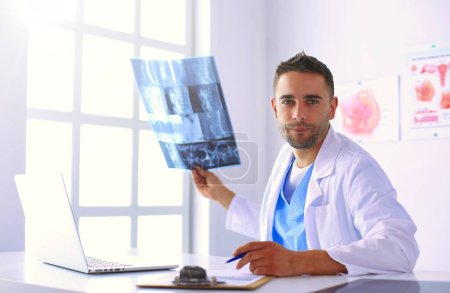 Photo for Portrait of a male doctor with laptop sitting at desk in medical office - Royalty Free Image