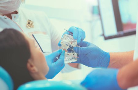 Téléchargez les photos : Dentiste chevronné au cabinet dentaire parlant avec une patiente et se préparant au traitement. - en image libre de droit