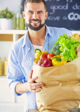 Téléchargez les photos : Homme tenant sac en papier plein d'épicerie sur le fond de la cuisine. Shopping et concept d'alimentation saine. - en image libre de droit