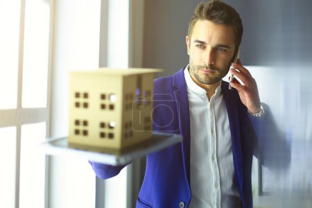 Photo for Businessman holding house miniature on hand standing in office - Royalty Free Image