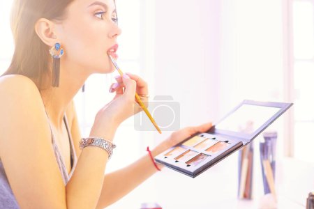 Téléchargez les photos : Brunette femme appliquant maquillage pour une date de soirée devant un miroir. - en image libre de droit