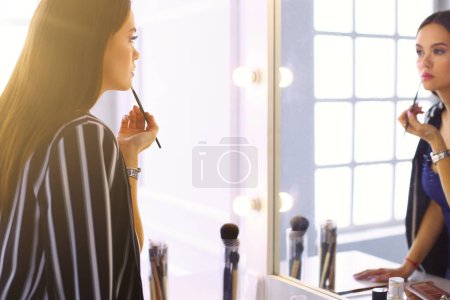 Photo for Young woman applying lipstick in front of a mirror. - Royalty Free Image