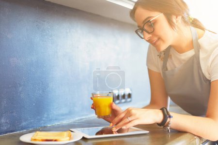 Téléchargez les photos : Portrait de jeune jolie femme au foyer brune caucasienne à la cuisine. Matin avec tasse de café et tablette pc. - en image libre de droit
