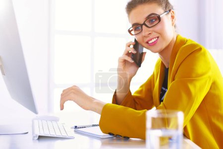 Photo for Businesswoman concentrating on work, using computer and cellphone in office. - Royalty Free Image