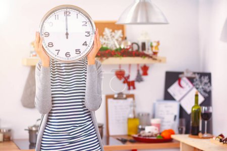 Téléchargez les photos : Joyeux jeune femme montrant horloge à Noël cuisine décorée . - en image libre de droit
