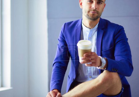 Téléchargez les photos : Jeune homme d'affaires assis isolé sur fond gris - en image libre de droit