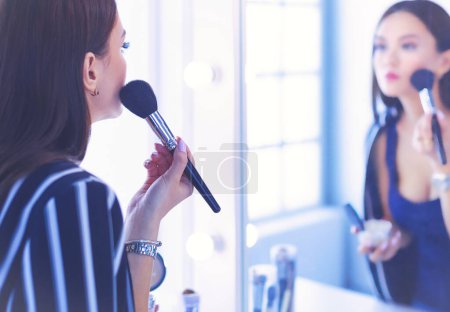 Téléchargez les photos : Belle fille regardant dans le miroir et appliquant cosmétique avec un gros pinceau. - en image libre de droit