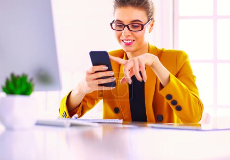 Téléchargez les photos : Portrait de femme d'affaires utilisant le téléphone portable et la messagerie texte alors qu'elle était assise au bureau devant un ordinateur portable - en image libre de droit