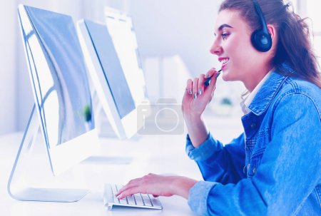 Téléchargez les photos : Femme d'affaires souriante avec casque à l'aide d'un ordinateur portable au bureau au travail - en image libre de droit