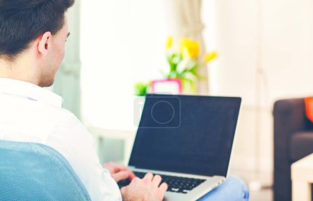 Téléchargez les photos : Homme heureux assis sur la table et utilisant un ordinateur portable à la maison
. - en image libre de droit