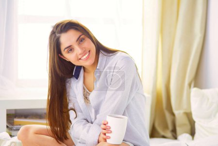 Photo for Woman sitting in bed reading a book and having breakfast. - Royalty Free Image