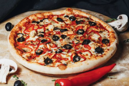 Pimienta recién horneadaUna deliciosa pizza entera con pepperoni, aceitunas y queso, adornada con chile rojo y champiñones.roni y pizza de aceituna en una mesa de madera rodeada de ingredientes. 
