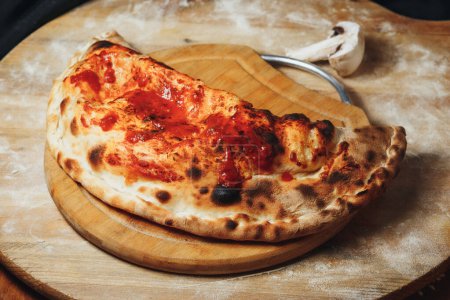 A golden-brown calzone filled with melted cheese and rich tomato sauce atop a circular wooden board.