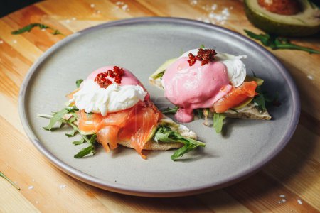 Two perfectly poached eggs sit atop smoked salmon and creamy avocado on a plate, drizzled with hollandaise sauce.