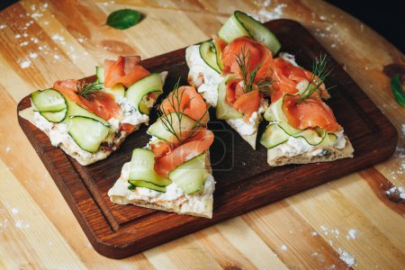 A slice of bread topped with vibrantly pink smoked salmon, crisp cucumber slices, and fragrant dill leaves in a delicious culinary arrangement.