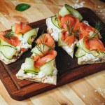 A slice of bread topped with vibrantly pink smoked salmon, crisp cucumber slices, and fragrant dill leaves in a delicious culinary arrangement.