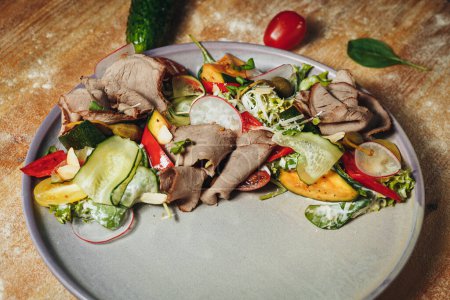 A plate filled with a variety of cooked meat and colorful vegetables, arranged on a rustic wooden table.