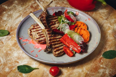 Succulent grilled lamb chops served with a colorful array of fresh vegetables on a white plate.