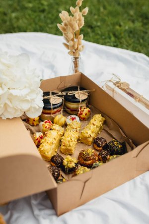 A charming picnic box brimming with an assortment of delectable pastries and fresh, colorful flowers, set against a natural backdrop.