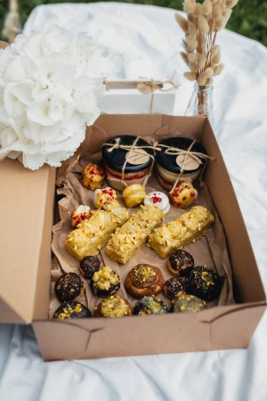 Foto de Una caja rebosante de una variedad de deliciosos pasteles rodeada de un vibrante surtido de flores frescas. - Imagen libre de derechos