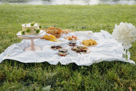 A colorful picnic blanket laid out with a variety of delicious foods, set against the serene backdrop of a lake on a sunny day.