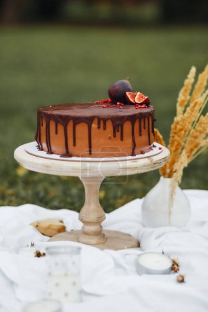A rich chocolate cake is placed on a wooden table in the midst of a beautiful field, surrounded by natures serenity.