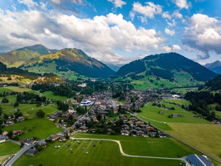Aerial shot of beautiful alpine landscape with town, hills and deep valleys. Picturesque golden hour in mountains. Gstaad, Switzerland.