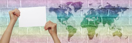 Photo for Rainbow coloured world map message placard template - hands holding blank sign against brick wall with map of world in graduated rainbow colours and space for copy - Royalty Free Image