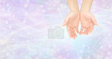 Téléchargez les photos : Les mains humbles d'un guérisseur Reiki - paire de mains ouvertes tasses femelles sur un fond éthérée étincelant rose pâle bleu brillant idéal pour un thème de guérison holistique spirituelle - en image libre de droit