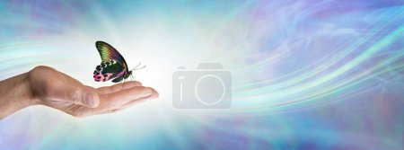 Téléchargez les photos : Moment spécial avec un fond de mémo message spirituel papillon papillon - papillon coloré assis sur la main ouverte d'un homme sur un fond d'énergie bleue fluide et l'espace de copie pour le texte - en image libre de droit