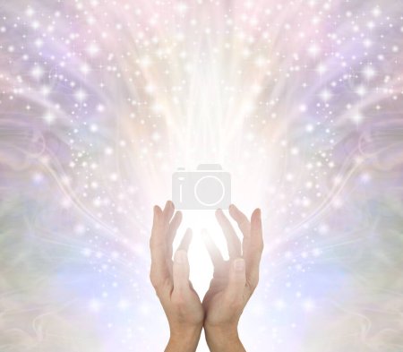 Sending you beautiful high vibe  healing energy - female cupped hands with white light and  sparkles flowing up and out on a pale wispy energy field background with copy space 
