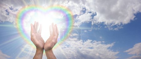 Foto de Enviándote bellas vibraciones sanadoras de inteligencia divina a través del éter - cielo azul y nubes esponjosas con un corazón lleno de luz de estrellas corazón de arco iris y manos masculinas enviando energía sanadora - Imagen libre de derechos