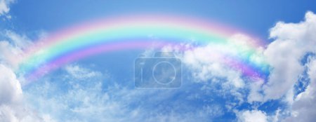Stunning wide blue sky and bright rainbow - big fluffy clouds with a giant arcing rainbow against a beautiful summer time blue sky with copy space for positive spiritual messages