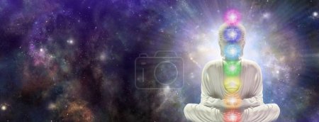Meditating Chakra Buddha sitting in lotus position surrounded by  deep space - buddha on right side with seven chakras against a starry dark blue celestial sky with a massive nebula and copy space for text 