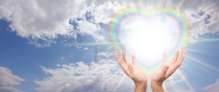 Foto de Enviándote vibraciones de sanación del corazón - cielo azul y nubes esponjosas con un corazón lleno de luz estelar corazón de arco iris y manos femeninas enviando energía sanadora - Imagen libre de derechos