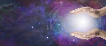 Téléchargez les photos : Travailler avec l'énergie de l'orbe de guérison cosmique mâle tenant une boule d'énergie entre ses mains parallèles ouvertes contre une vaste étendue d'espace profond avec espace de copie pour le message spirituel - en image libre de droit