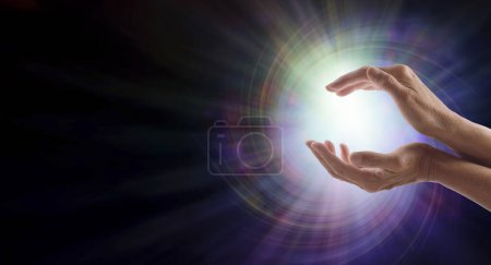 Photo for Sending Vortex Healing Energy Concept- female cupped hands with a beautiful white star burst orb  against a multicoloured energy vortex graduated to black background and copy space for spiritual message - Royalty Free Image