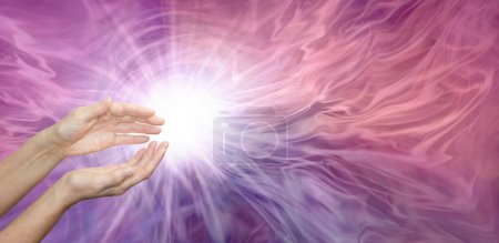 Beaming Reiki heart healing energy - Female cupped hands with bright white starlight at fingertips against a beautiful ethereal pink purple wispy background and copy space 