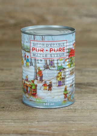 Photo for St-EPHREM, QUEBEC, CANADA - APRIL 2, 2023.  New 2023 can of Pure Canadian Maple syrup with vintage illustration on a wooden table. Quebec is the largest maple syrup producer in the world.  Text in french and english. - Royalty Free Image