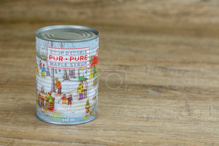 Photo for St-EPHREM, QUEBEC, CANADA - APRIL 2, 2023.  New 2023 can of Pure Canadian Maple syrup with vintage illustration on wooden table. Quebec is the largest maple syrup producer in the world.  Text in french and english. Landscape, horizontal, left. - Royalty Free Image