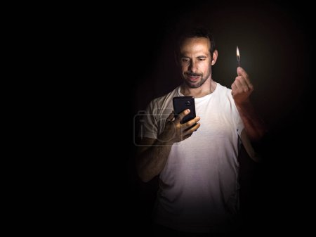 Foto de Hombre mirando su celular con una cerilla en la oscuridad. Concepto de apagón. Enfoque selectivo. - Imagen libre de derechos