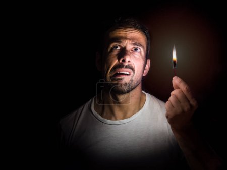 Foto de Worried man with a match in the dark. Blackout concept. - Imagen libre de derechos