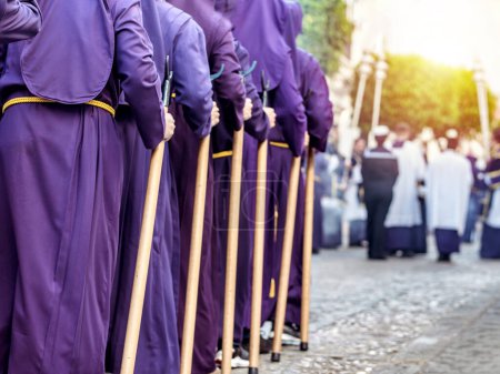 Menschen in lila Gewändern und gelben Gürteln mit Holzstäben während einer Prozession. Selektiver Fokus.