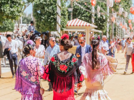 Seville, Spain - April 26, 2023 : Women in colorful flamenco dresses at the festive Seville Fair.