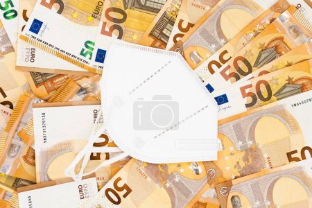 A white face mask, symbolizing the COVID-19 pandemic, rests on a spread of 50 Euro banknotes, representing the economic implications.