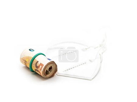 A roll of banknotes secured with a green band, lying on a white KN95 face mask