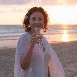 A figure savors wine, gazing at a tranquil beach sunset.
